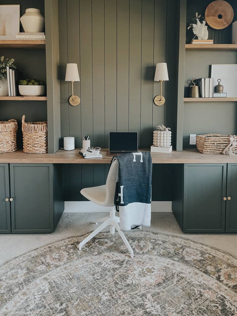 green home office with cabinets on the ground, a bookshelf above and a desktop in between. the green is a rich mossy green that compliments the cream of the office chair.