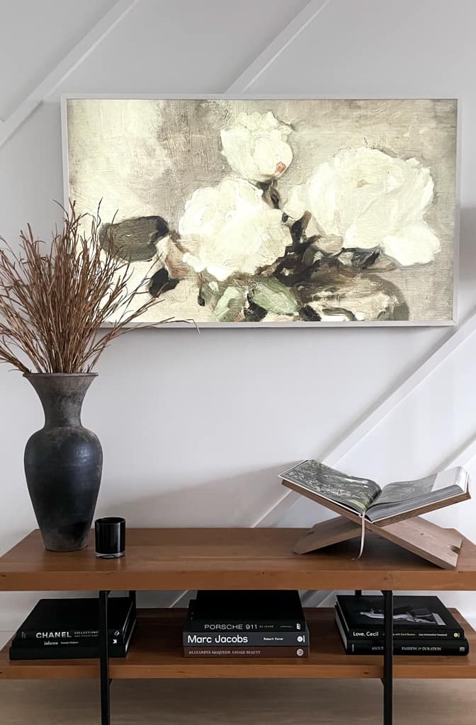 Book display sitting on top of a console table next to a vase and candle above some books and an art piece on the samsung frame TV