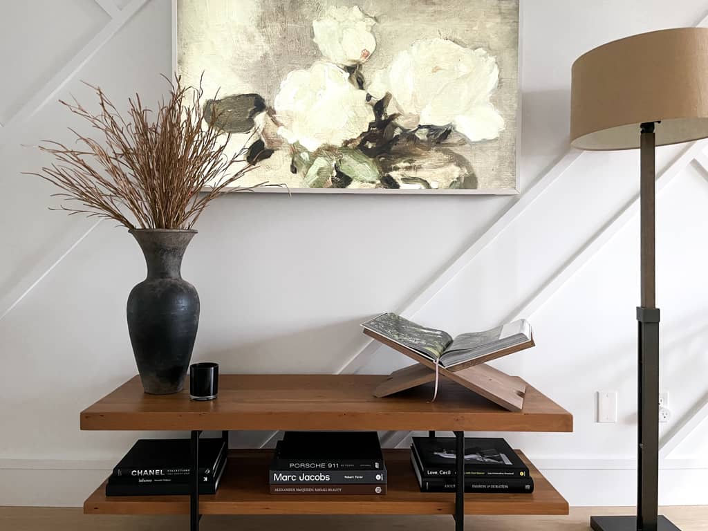 Book display sitting on top of a console table next to a vase and candle above some books and an art piece on the samsung frame TV