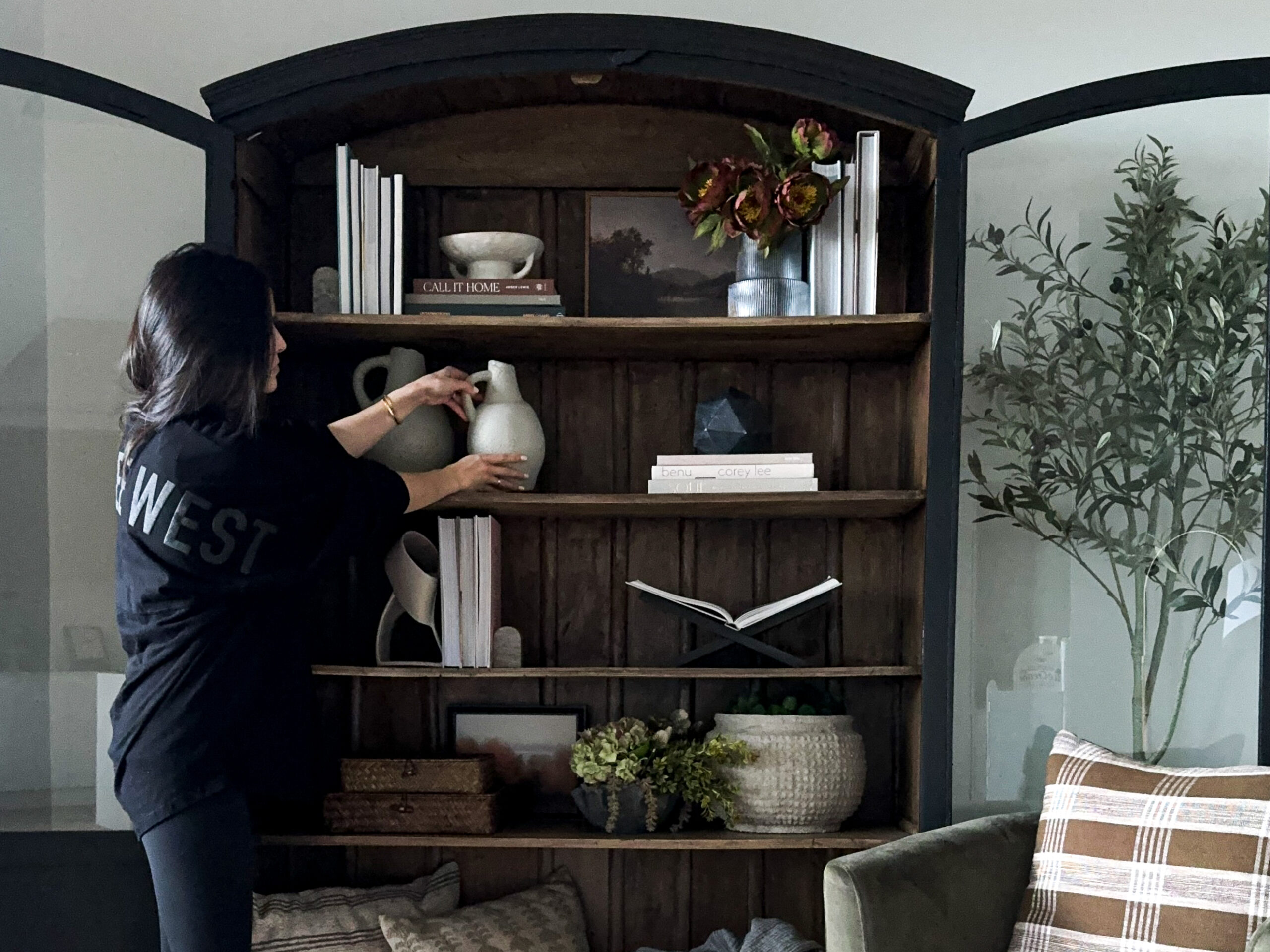 signed samantha styling shelves in her black arched cabinet. the shelves have books, plants, vases, and other decorative objects on it.