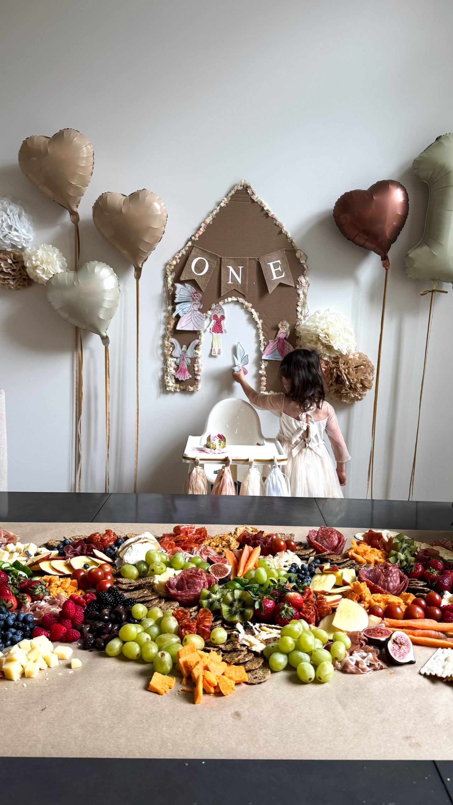 Dog themed first birthday set up with a charcuterie boar don the table, dog blow up balloons, a cardboard dog house, and balloons on the wall.