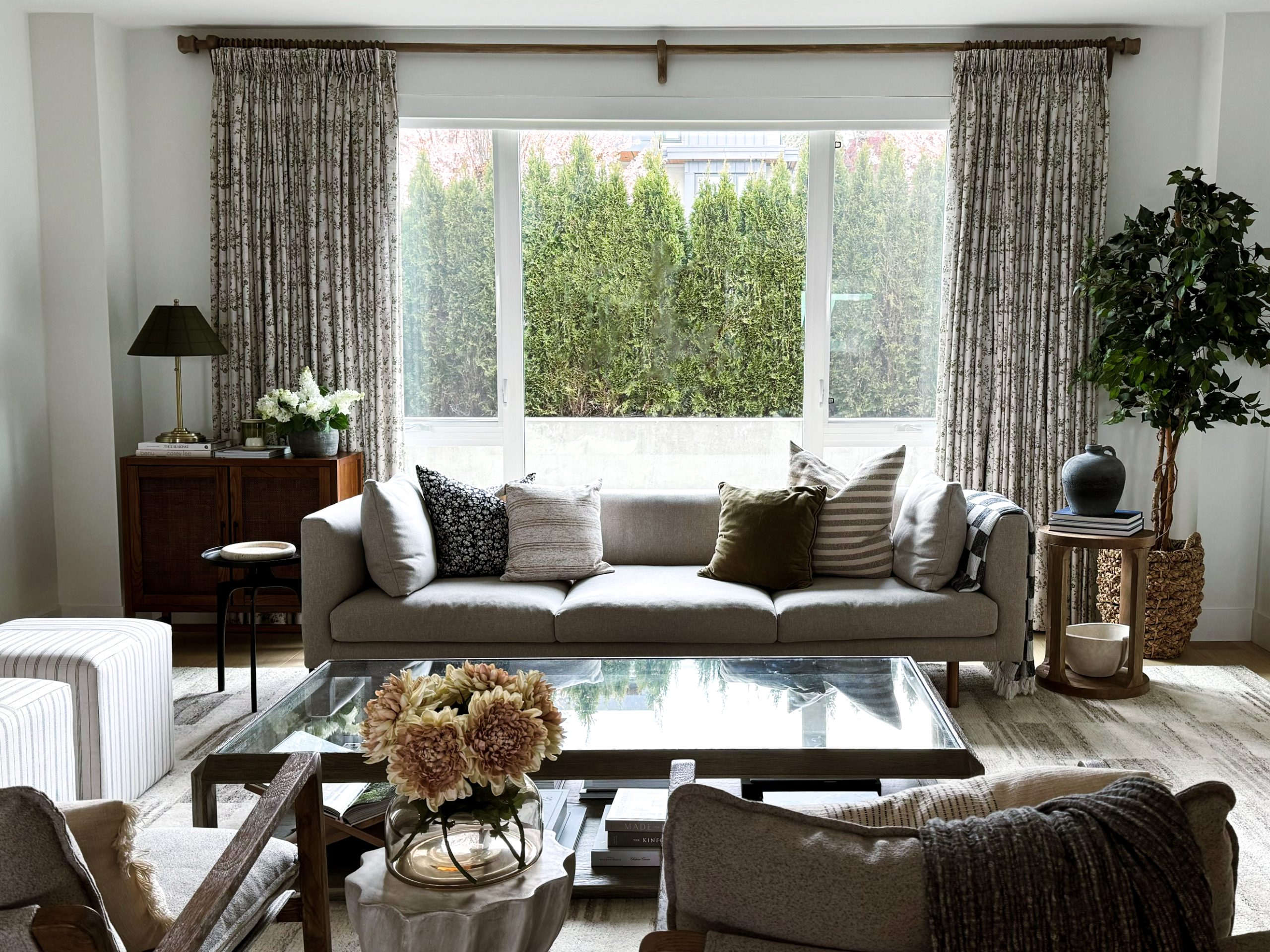 Two pages curtains in a hanging bordering a larger window in a living room - the Sara Le collection with whimsical florals in greens and a neutral beige as the background