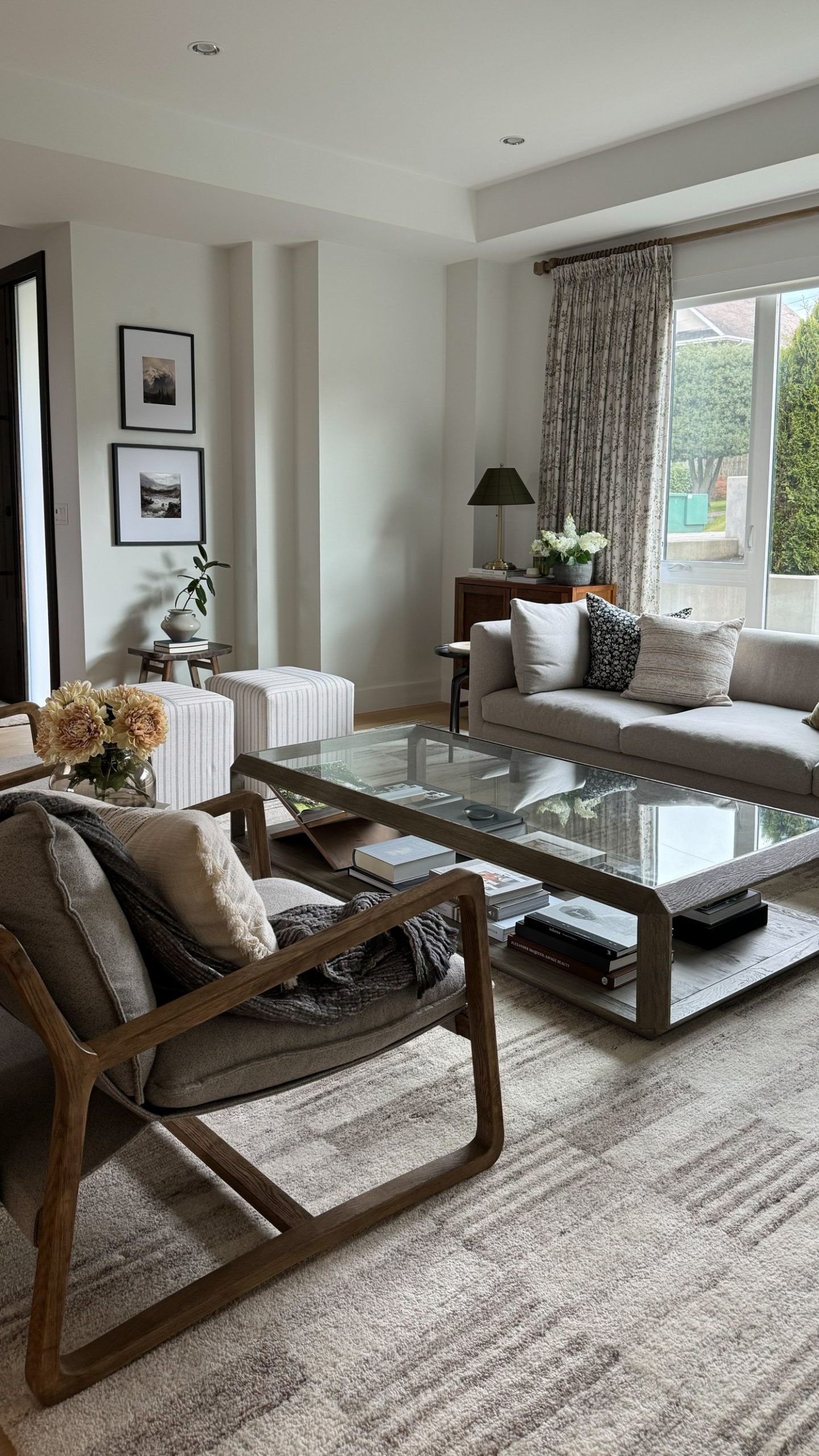 Two pages curtains in a hanging bordering a larger window in a living room - the Sara Le collection with whimsical florals in greens and a neutral beige as the background