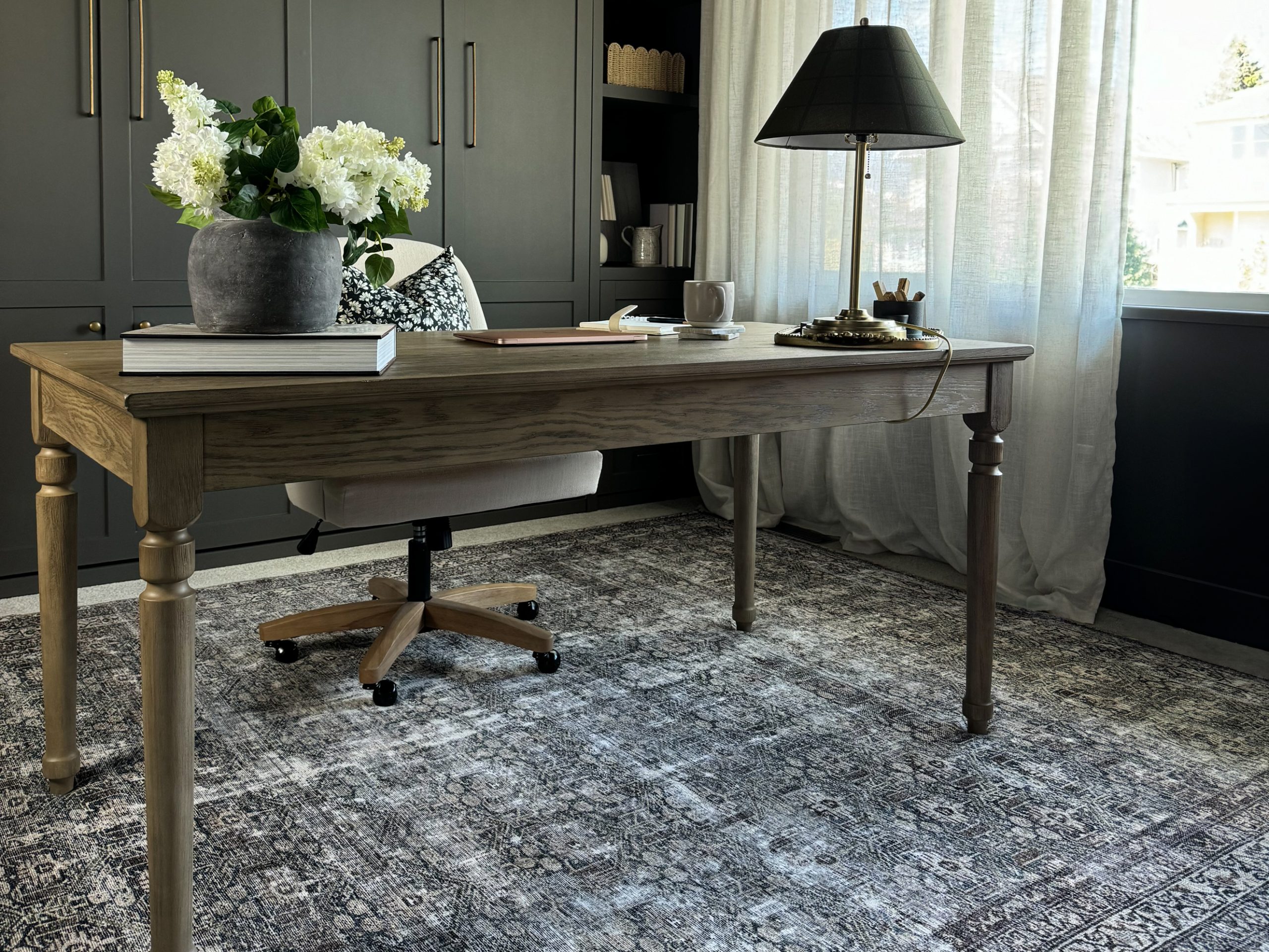 a desk in the middle of an office with a lamp chair and flowers on it