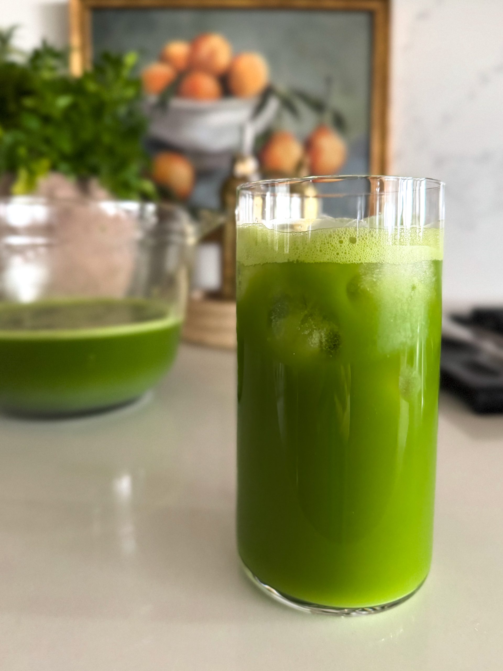 a delicious looking green juice in a glass and a measuring cup in front of a plant and picture