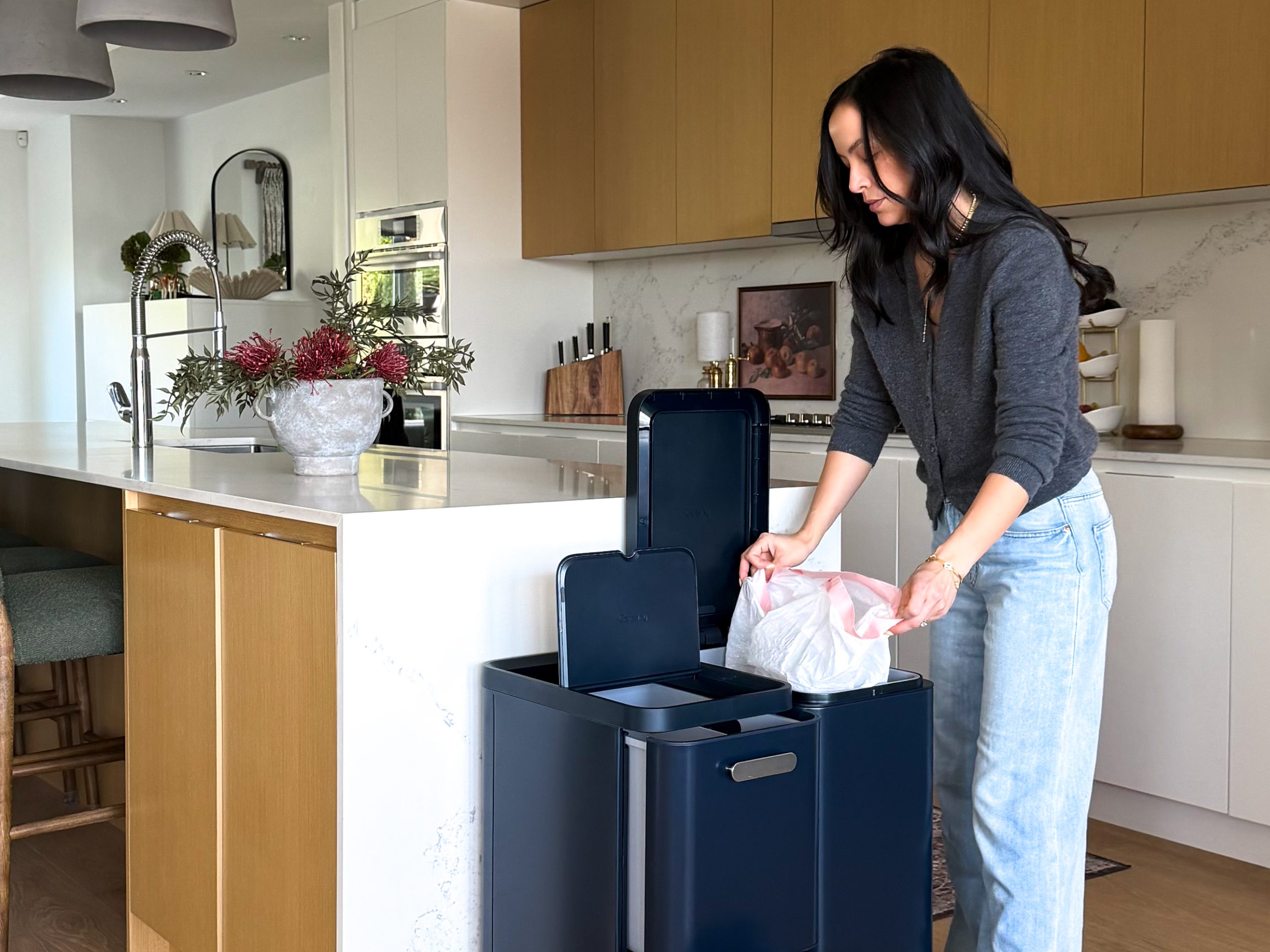 woman adding trash bag to Caraway's new trash bins in navy blue .