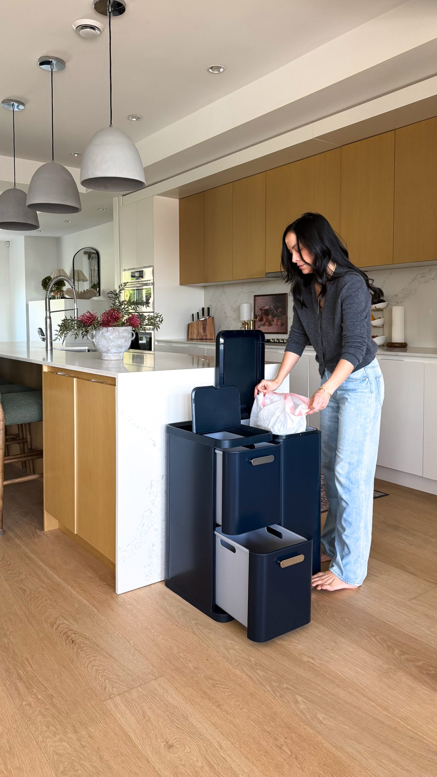 woman adding trash bag to Caraway's new trash bins in navy blue .